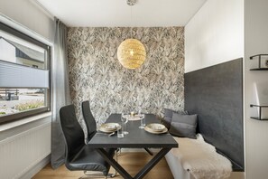 A modern dining area with a black table, two chairs, and a decorative light fixture.