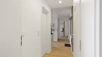 A corridor with white walls and wooden flooring leading to a kitchen area.