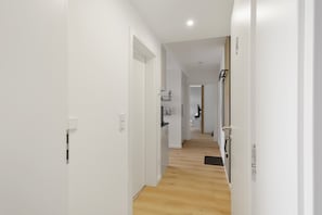 A corridor with white walls and wooden flooring leading to a kitchen area.