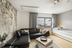 Uma sala de estar moderna com um sofá de couro preto, uma mesa de centro branca e vista para o exterior através de uma grande janela.