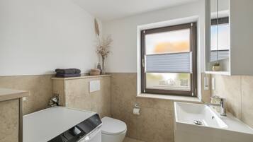 Een moderne badkamer met een wasmachine, toilet, wastafel en een raam met zonwering.