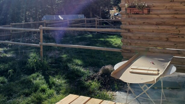 A wooden cabin with a deck, a table, and chairs, overlooking a mountainous landscape. - Spacious apartment with a south-facing garden and terraces (Le Monêtier-les-Bains)