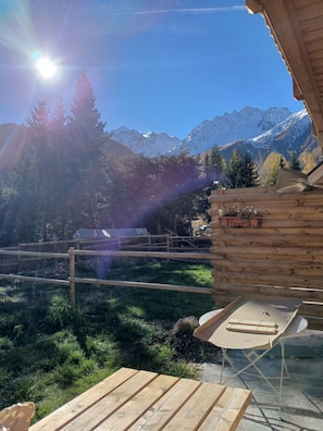 A wooden cabin with a deck, a table, and chairs, overlooking a mountainous landscape. - Spacious apartment with a south-facing garden and terraces (Le Monêtier-les-Bains)
