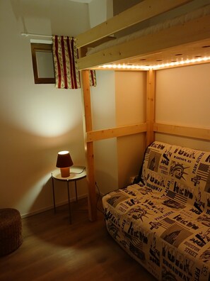 Un lit superposé avec une couverture à motifs, une petite table avec une lampe et une fenêtre avec des rideaux.