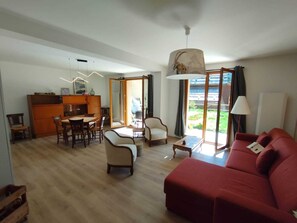 A living room with a red sofa, a dining area with a table and chairs, and a kitchen area with a wooden cabinet. - Spacious apartment with a south-facing garden and terraces (Le Monêtier-les-Bains)