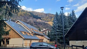A building with a sloped roof, a car parked in front, and a mountainous backdrop. - Spacious apartment with a south-facing garden and terraces (Le Monêtier-les-Bains)