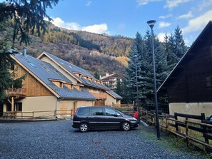 Ein Gebäude mit geneigtem Dach, ein geparktes Auto davor und eine Berglandschaft im Hintergrund.