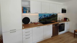 A modern kitchen with white cabinetry, a wooden countertop, a built-in microwave, and a large window with a mountain view. - Spacious apartment with a south-facing garden and terraces (Le Monêtier-les-Bains)