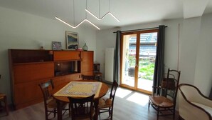 A dining area with a wooden table and chairs, a cabinet, and a view through a sliding glass door to a garden. - Spacious apartment with a south-facing garden and terraces (Le Monêtier-les-Bains)