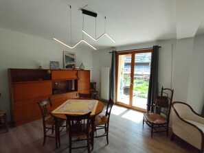 Ein Essbereich mit Holztisch und -stühlen, einem Schrank und Blick durch eine Schiebetür in einen Garten.