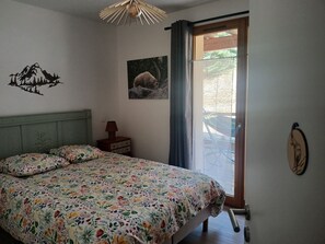Ein Schlafzimmer mit einem Bett, einem Nachttisch, einer Wandlampe, einem Fenster mit Vorhängen und einer Tür.
