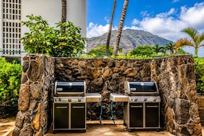 Zwei Weber-Grills mit Seitenschränken vor einer Steinwand mit Blick auf die Berge.