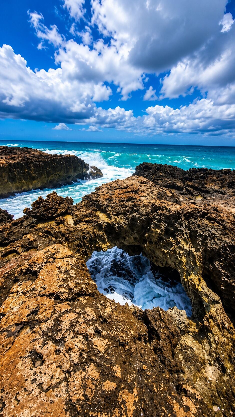 A rocky coastline with waves crashing against the rocks under a partly cloudy sky.
