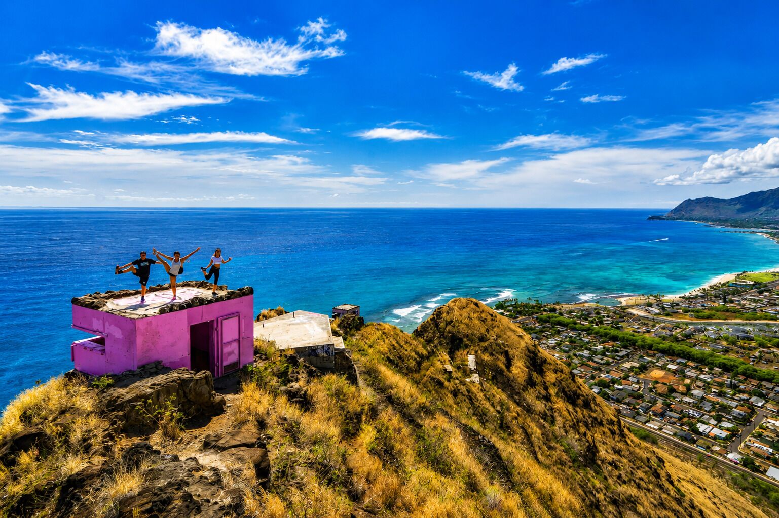 Una estructura rosa en un acantilado con vista a un pueblo costero bajo cielos azules y despejados.