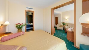 A hotel room with a bed, a desk, a chair, a mirror, and a door leading to another room. - Hotel Palas (Constanța)