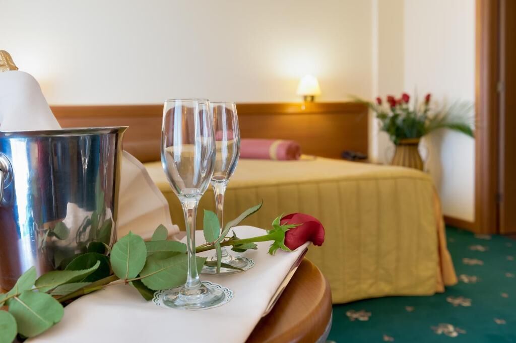A neatly arranged hotel room with a bed, a bedside table with a lamp, and a bouquet of flowers.