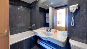 A modern bathroom with a large mirror, a bathtub, a sink with two faucets, and a hairdryer mounted on the wall. - Hotel Palas (Constanța)