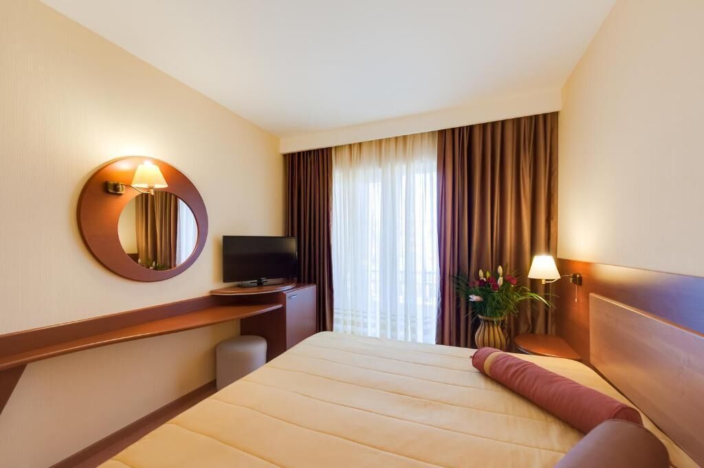 Une chambre d’hôtel avec un lit, une télévision, un bureau et une fenêtre avec des rideaux.