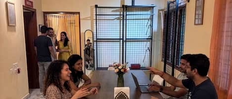A conference room with a wooden table, white chairs, a ceiling fan, and a large window with blinds.