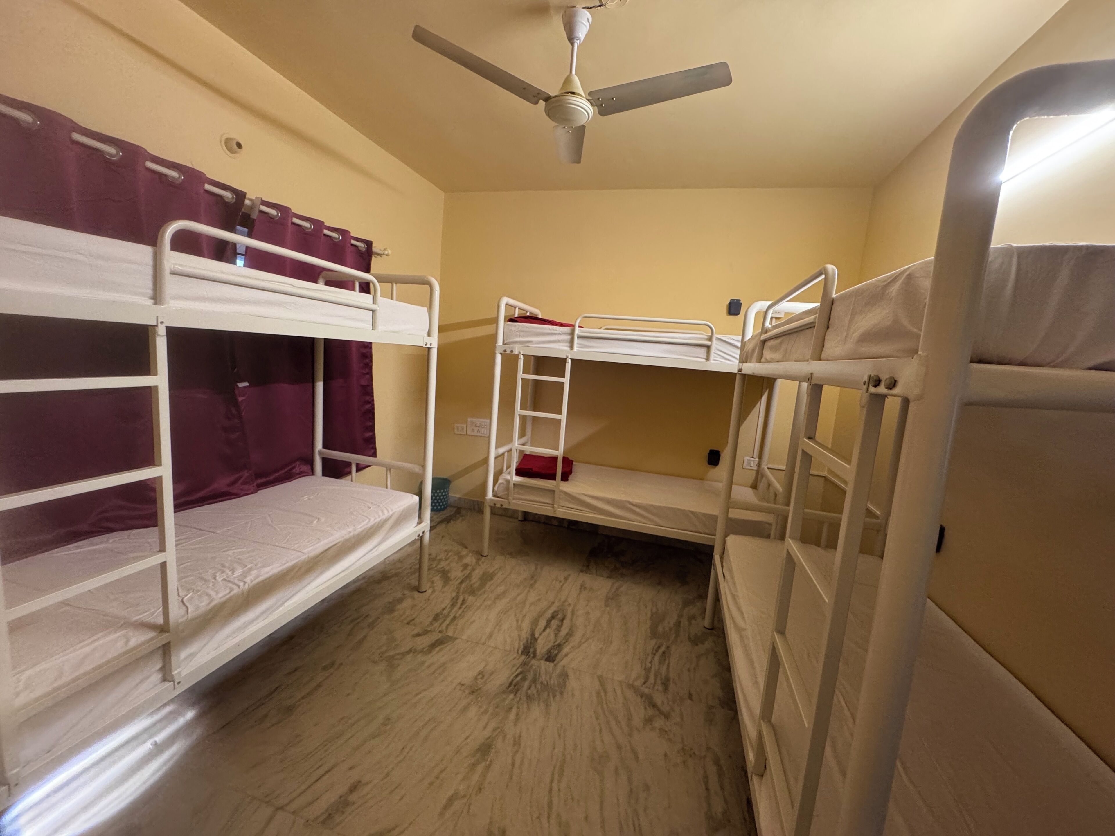 A bunk bed room with a ceiling fan, a window with purple curtains, and a wooden floor.