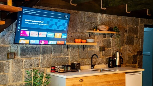 Una cocina con pared de piedra, estantes de madera, un lavamanos y un televisor montado mostrando una interfaz de YouTube.