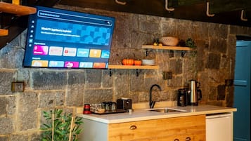 Een keuken met een stenen muur, houten planken, een gootsteen en een aan de muur bevestigde televisie waarop een YouTube-interface wordt weergegeven.