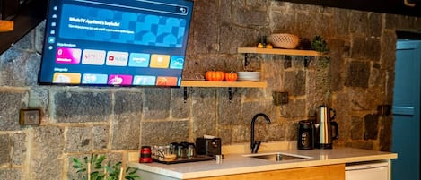A kitchen with a stone wall, wooden shelves, a sink, and a mounted TV displaying a YouTube interface.