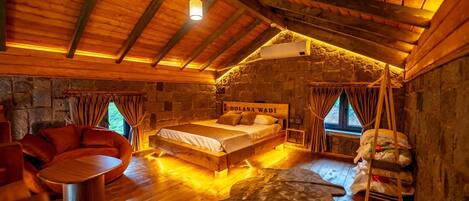 A cozy room with a bed, a wooden table, and a stone wall.