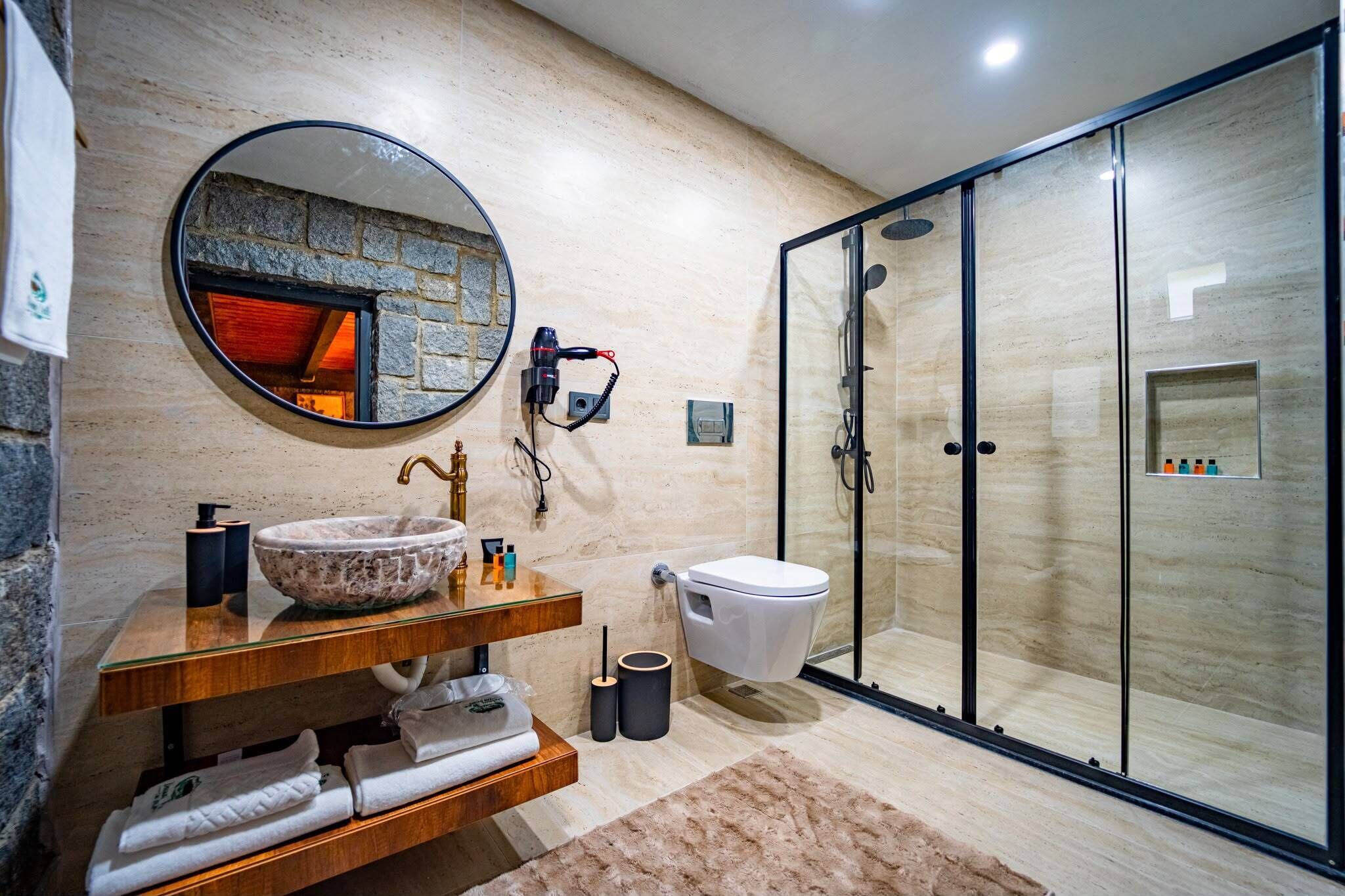 Un bagno moderno con lavabo in pietra, uno specchio rotondo, box doccia in vetro e un water.