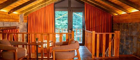 Un chalet confortable avec un intérieur en bois, une cheminée en pierre et un balcon agrémenté de rideaux.