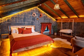 A cozy attic bedroom with a stone wall, a wooden bed, a hanging chair, and a window with red curtains. - Dolana Wadi Taş Evleri (Ardeşen)
