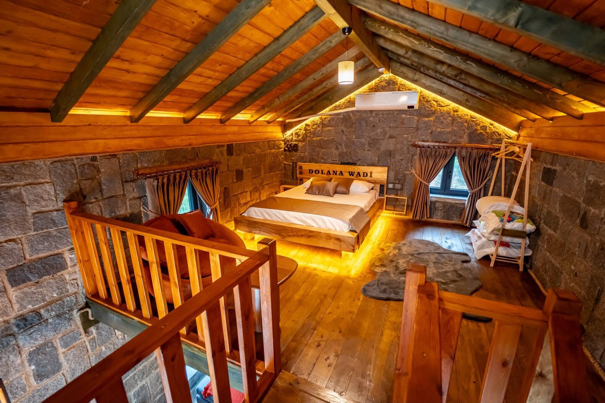 Een gezellige zolderkamer met een bed, houten balken, stenen muren en een klein balkon.