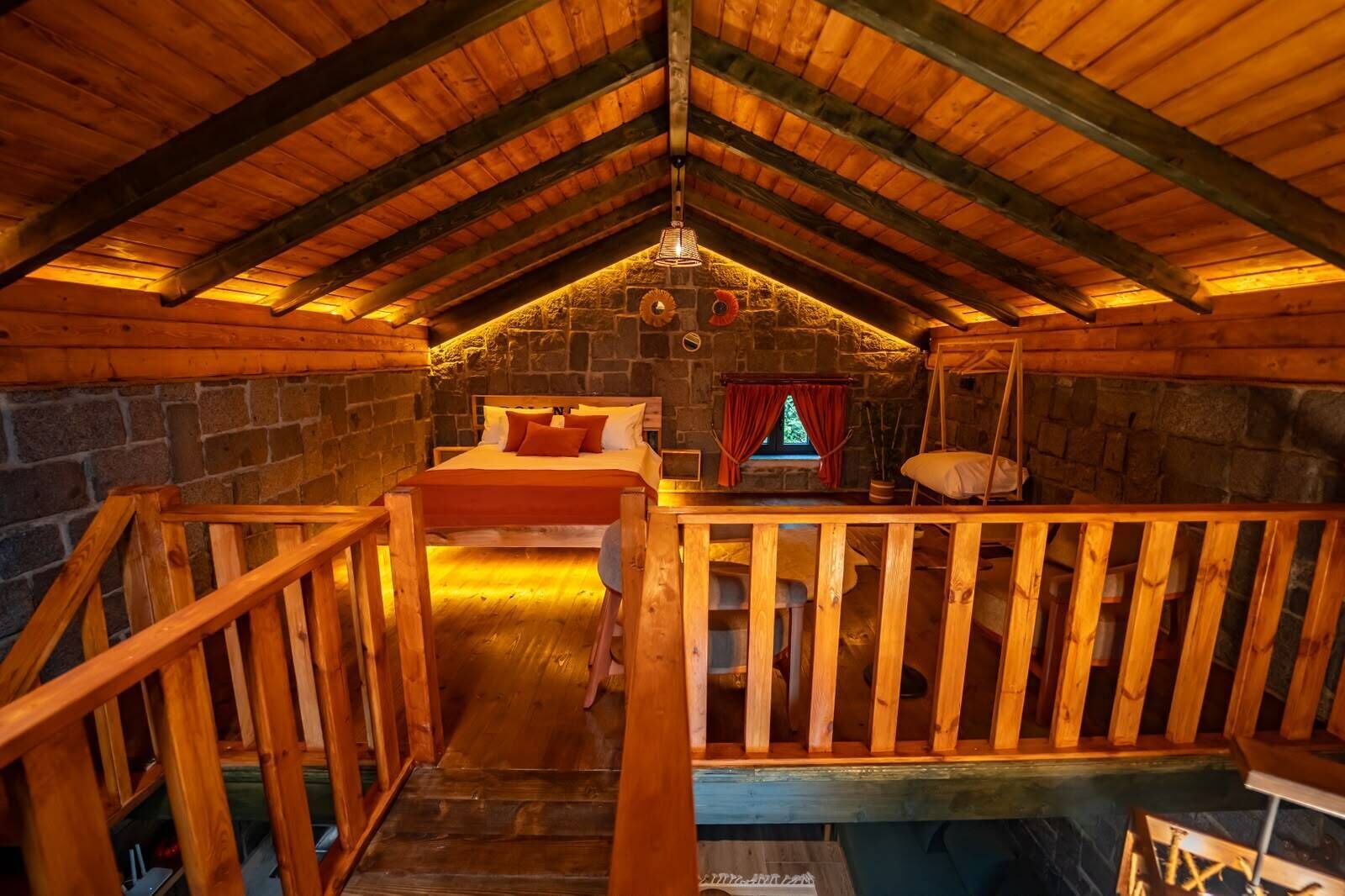 A cozy attic bedroom with a wooden ceiling, stone walls, a bed, and a small window.