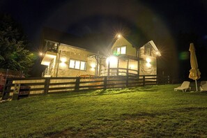 A two-story building with a wooden fence, outdoor seating, and a well-lit exterior at night.