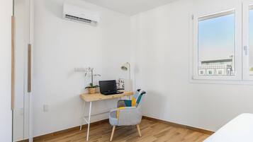 Ein Zimmer mit einem Holztisch, einem Laptop, einem Stuhl, einer Klimaanlage und einem Fenster mit Blick.