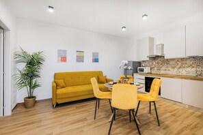 Un espace de vie moderne comprenant un canapé, une table à manger, des chaises, une plante en pot et un coin cuisine avec un four à micro-ondes.