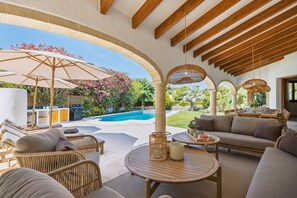 An outdoor patio with wicker furniture, a round table, and a pool in the background. - Casa Hero - Javea, Costa Blanca (Javea)