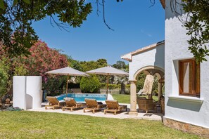 A pool area with lounge chairs and umbrellas, surrounded by greenery and a white building. - Casa Hero - Javea, Costa Blanca (Javea)