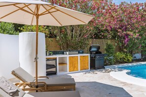 A poolside area with a built-in barbecue, a lounge chair, and a wooden fence. - Casa Hero - Javea, Costa Blanca (Javea)