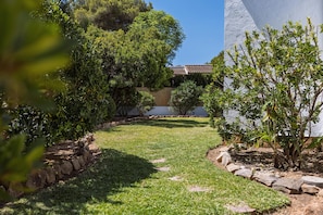 Ein Garten mit einem gepflasterten Weg, üppiger Vegetation und einem Gebäude mit einem Ziegeldach.