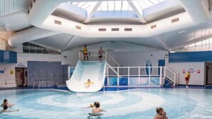 An indoor swimming pool with a central slide, multiple lanes, and a high ceiling with skylights. - Cosy seaside adventure home sweet home (Poole)