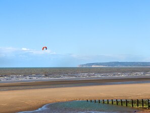 A beach with a sandy shore, a wooden fence, and a person flying a kite in the distance.