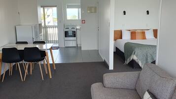 A modern, well-lit room with a dining area, kitchenette, and a bed with a view.