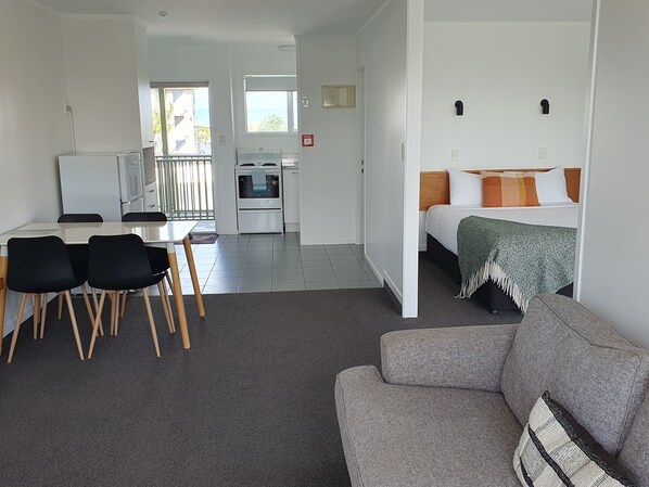 A modern, well-lit room with a dining area, kitchenette, and a bed with a view.