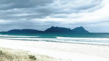 A beach with white sand and a view of mountains in the distance under a cloudy sky.