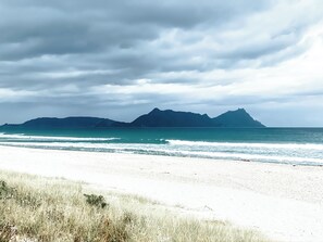 A beach with white sand and a view of mountains in the distance under a cloudy sky.