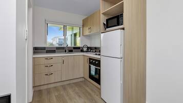 A modern kitchen with wooden cabinets, a white refrigerator, a microwave, and a kettle on the counter.