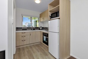 A modern kitchen with wooden cabinets, a white refrigerator, a microwave, and a kettle on the counter.