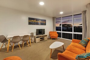 A modern living room with a television, seating area, and a large window with a cityscape view.