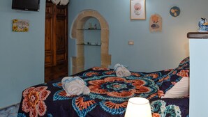 Un dormitorio con una cama, un armario de madera, un arco de piedra y un televisor fijado a la pared.